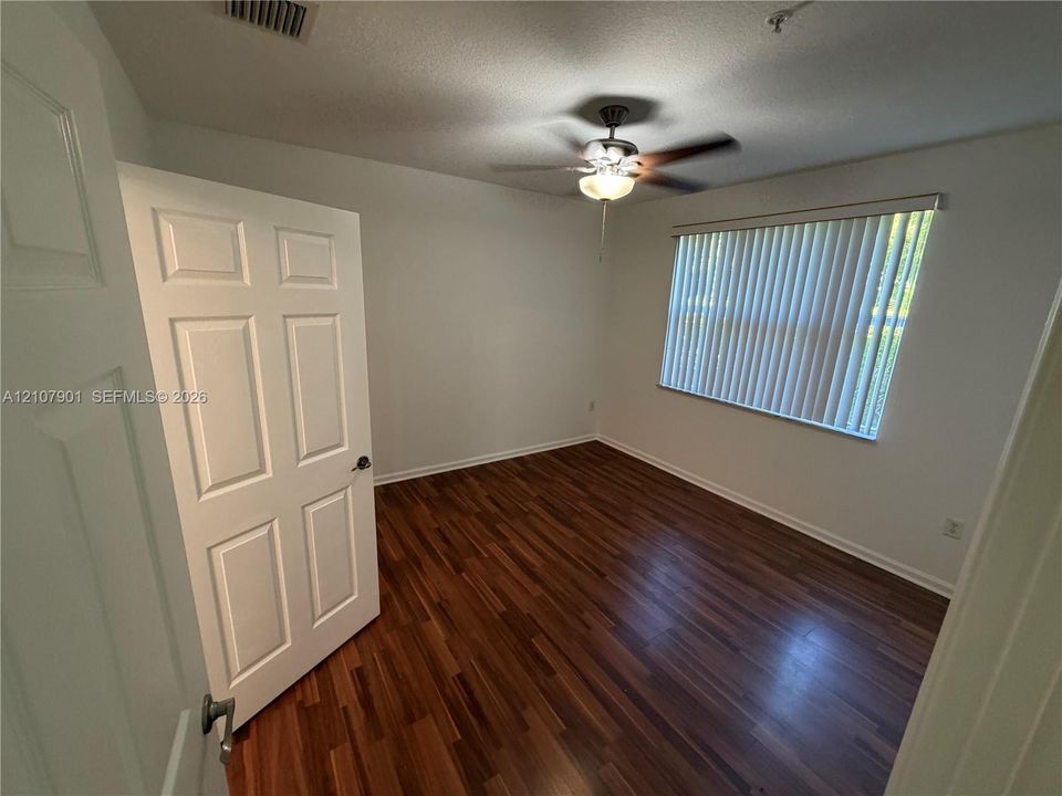 Room featuring wood-finish flooring, a multi-panel door, and a ceiling fan with integrated lighting