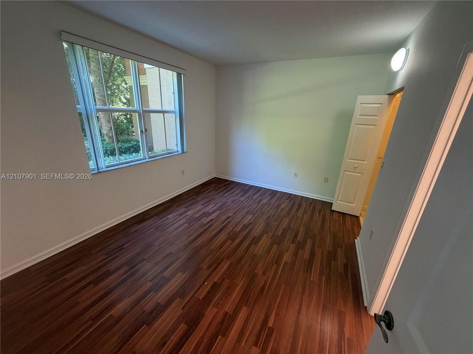 Wood-finish flooring, large window with horizontal blinds, neutral wall paint, and a bi-fold closet door
