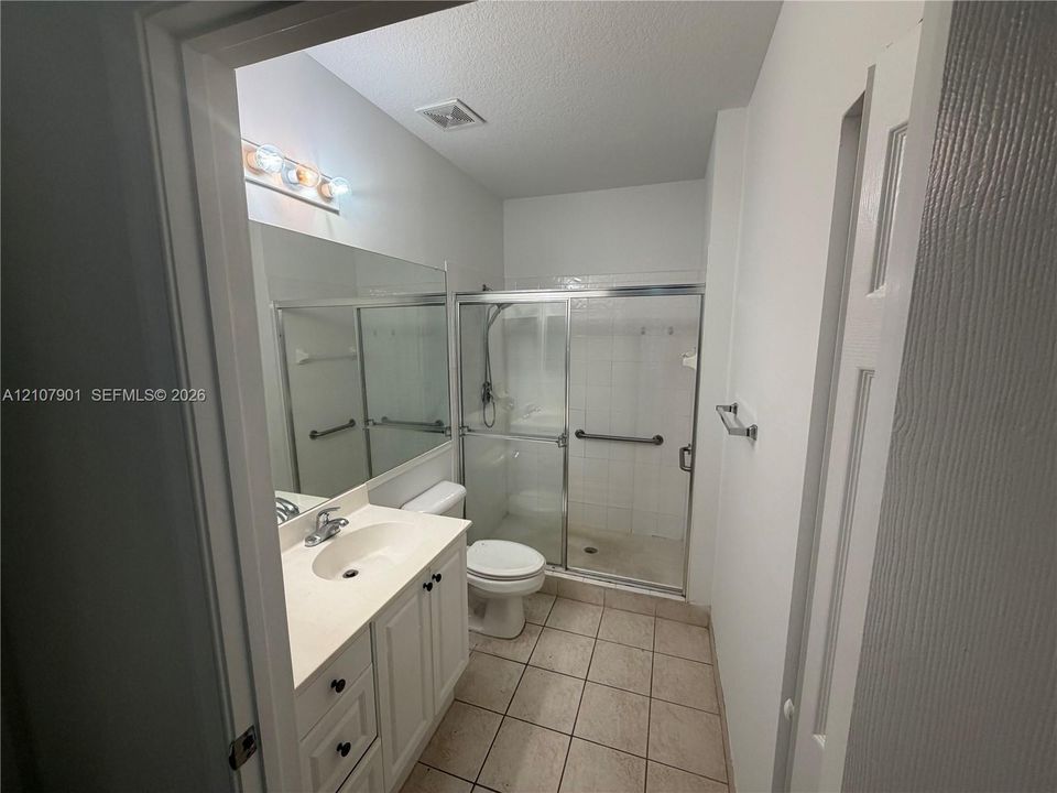 Bathroom featuring a vanity with white cabinetry, a single-basin countertop, a full-width mirror, and a walk-in shower with glass sliding doors and tile surround