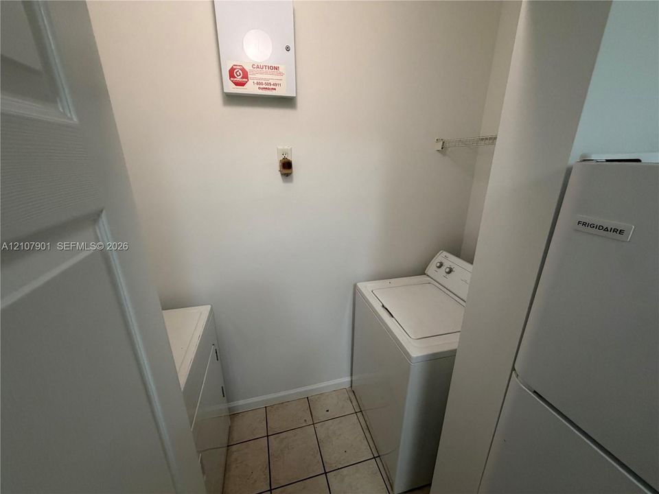 Utility area featuring tile flooring, white-finish appliances, and a wall-mounted shelving unit