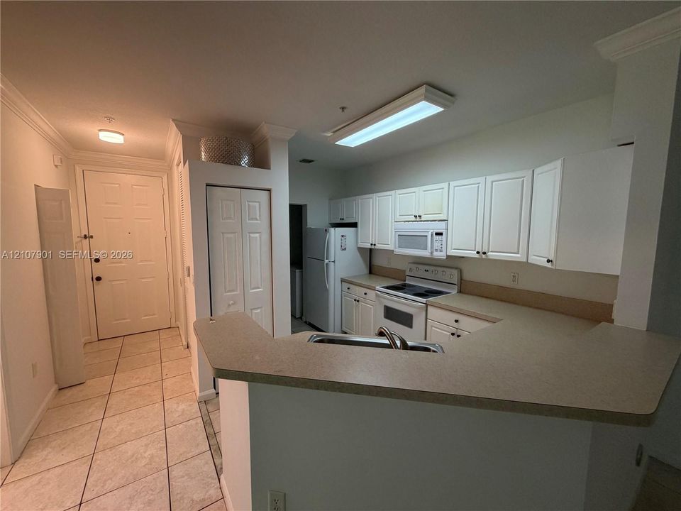 Kitchen featuring white cabinetry, solid-surface countertops, tile flooring, integrated appliances, and a breakfast bar