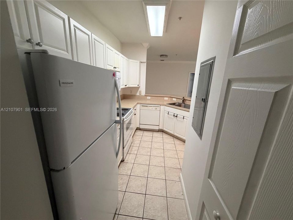 Kitchen featuring white cabinetry, solid-surface countertops, tile flooring, and integrated white appliances