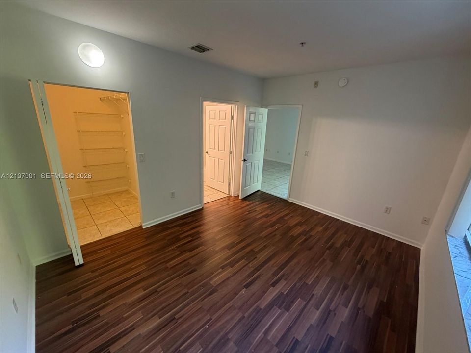Room featuring wood-finish flooring, a walk-in closet with built-in wire shelving, and tile flooring in the entryways