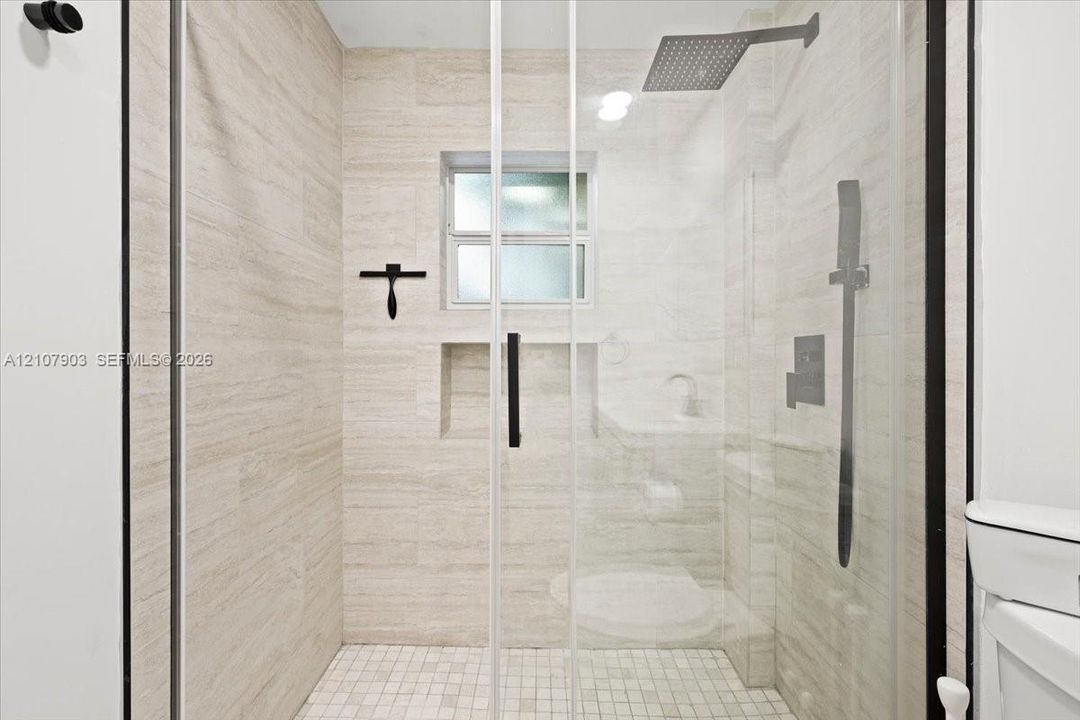 Walk-in shower featuring floor-to-ceiling stone-finish tile, glass enclosure, recessed storage niche, overhead rainfall showerhead, and a mosaic tile floor