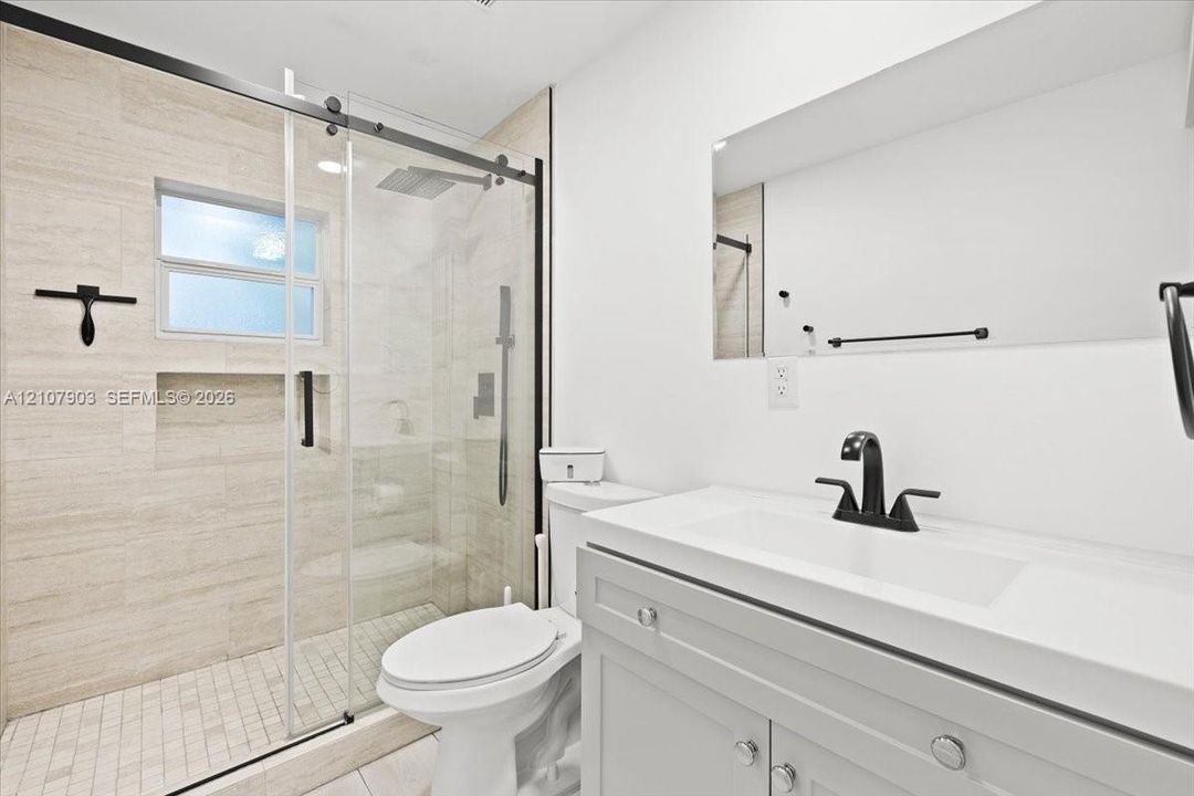 Bathroom featuring a glass-enclosed walk-in shower with horizontal stone-style wall tile and built-in recessed shelving, a vanity with a rectangular integrated sink, matte black hardware, and a frameless wall-mounted mirror