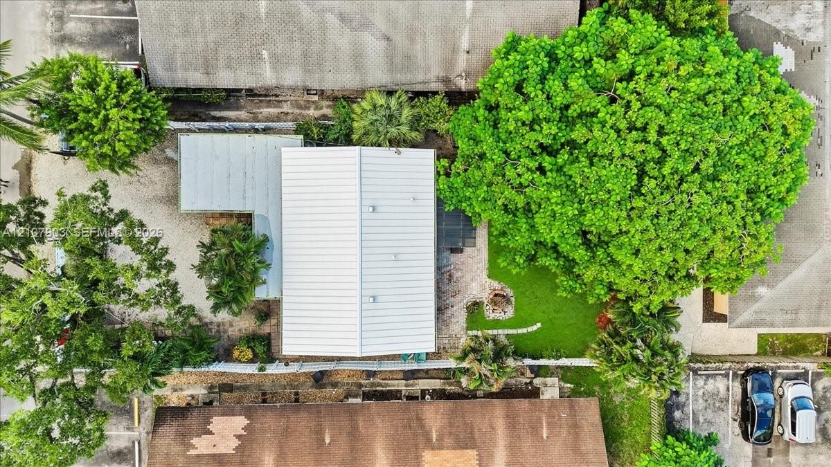 Aerial perspective featuring a metal roof structure, manicured lawn, established canopy trees, and paved parking area