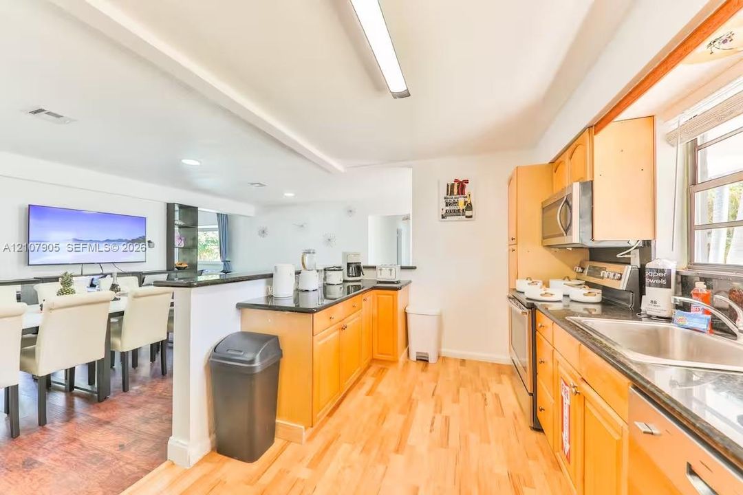 Kitchen featuring wood cabinetry, dark stone-finish countertops, stainless steel appliances, and wood-finish flooring