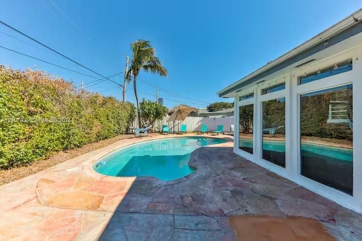 Free-form swimming pool with stone-style paver patio, expansive privacy hedging, and floor-to-ceiling windows