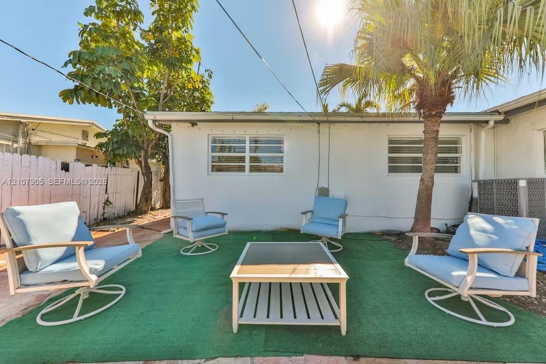 Exterior patio area featuring a white stucco facade, horizontal slat windows, and a mature palm tree