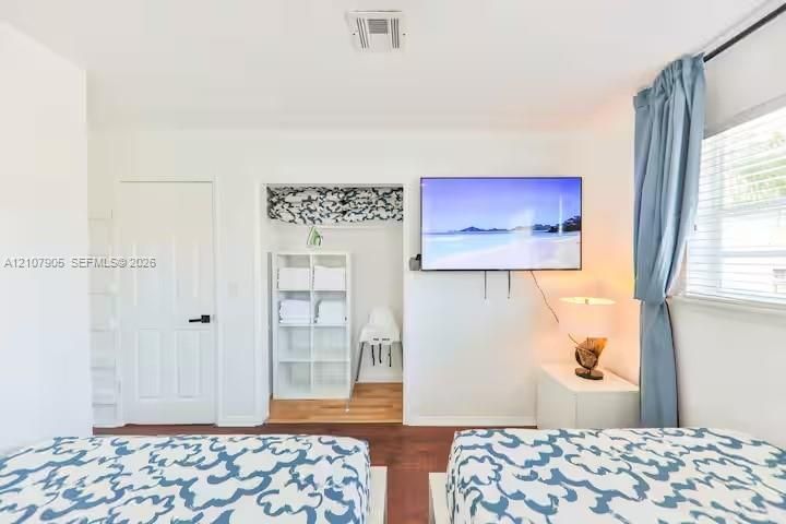 Interior space featuring wood-finish flooring, a recessed closet with built-in shelving, a solid-core door with matte black hardware, and window horizontal blinds