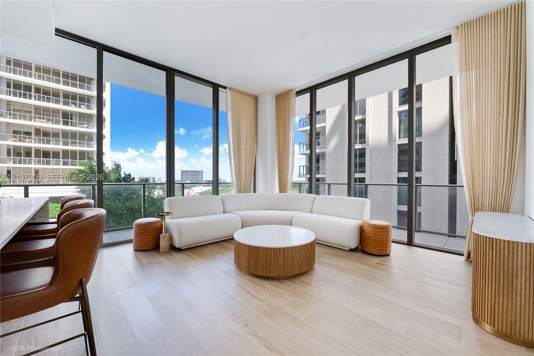 Floor-to-ceiling glass windows, wide-plank wood-finish flooring, and a private balcony with glass railing