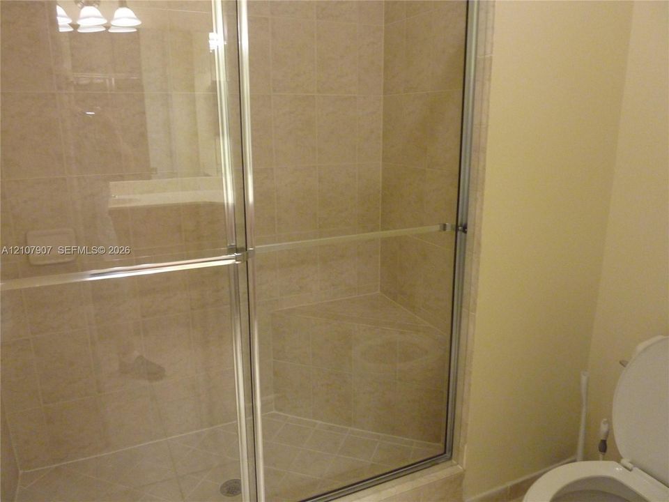 Walk-in shower featuring a built-in tiled bench, glass sliding enclosure, and neutral-toned wall tile