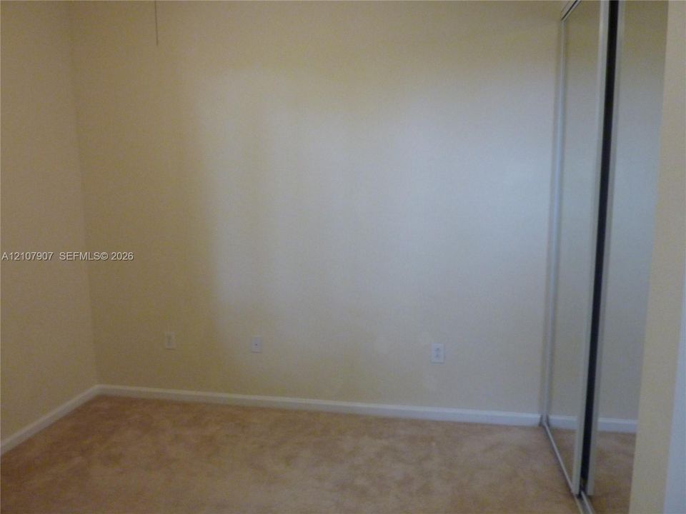 Neutral-toned interior space featuring wall-to-wall carpeting and a floor-to-ceiling mirrored sliding-door closet