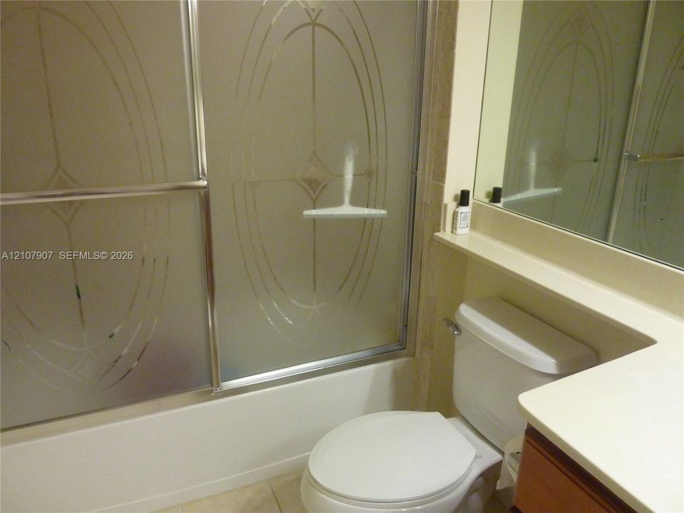Bathroom featuring a shower enclosure with frosted glass sliding doors, a solid-surface vanity countertop, a wall-to-wall mirror, and neutral floor tile
