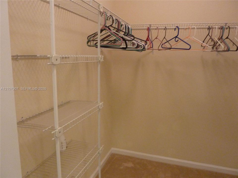 Walk-in closet featuring white wire shelving units and integrated clothing rods