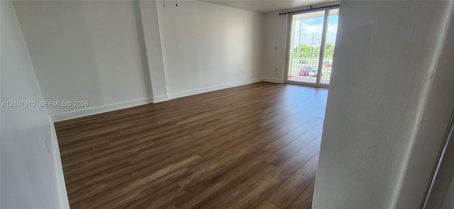 Open living area featuring wood-finish flooring, smooth-finish walls, and a glass sliding door providing exterior access