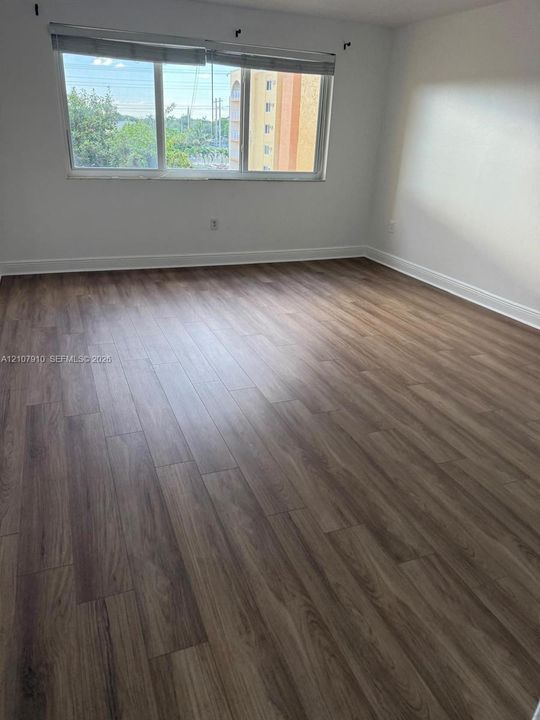 Interior space featuring wood-finish flooring, neutral wall tones, and a large window with a roller shade