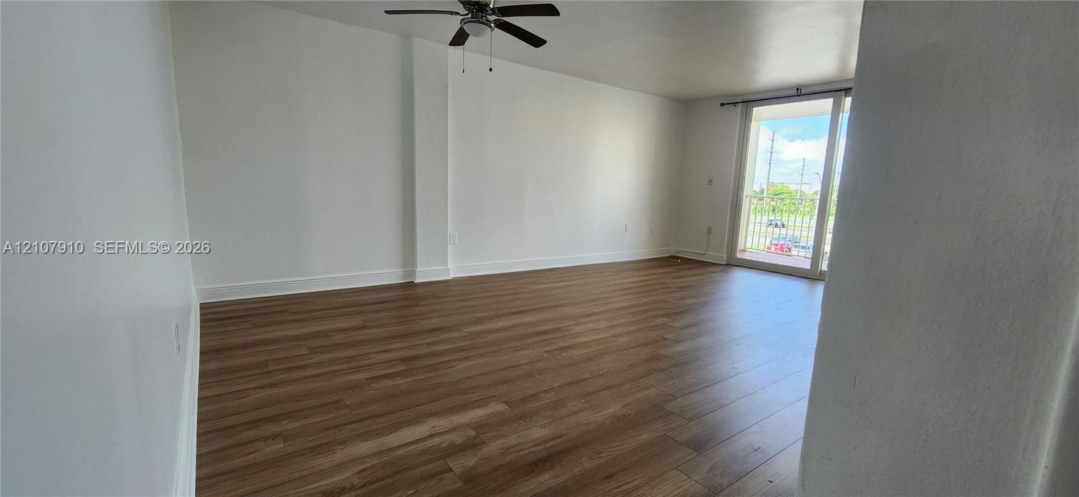 Open-concept living space featuring wood-finish flooring, white walls, a ceiling fan, and sliding glass doors to a balcony