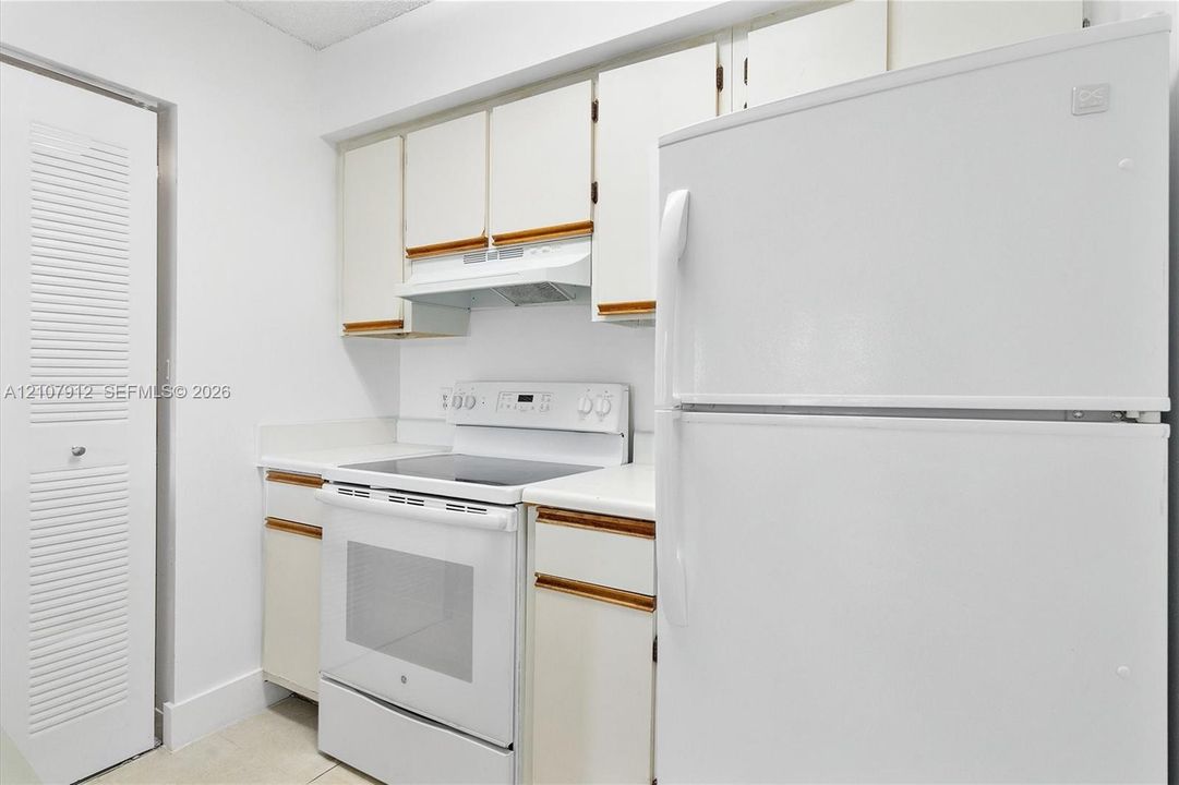 Kitchen featuring white cabinetry with wood trim, a built-in exhaust hood, a white electric range, a full-sized refrigerator, and a louvered-door closet