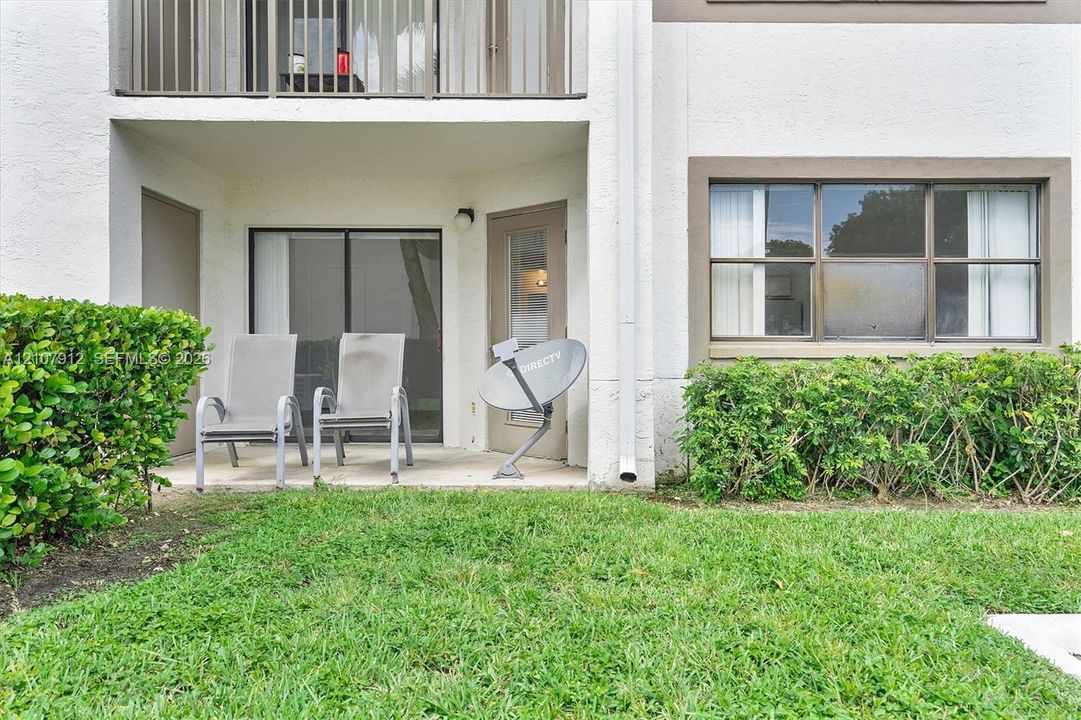 Ground-level concrete patio featuring sliding glass doors, an exterior door with glass inlay, and an upper-level balcony