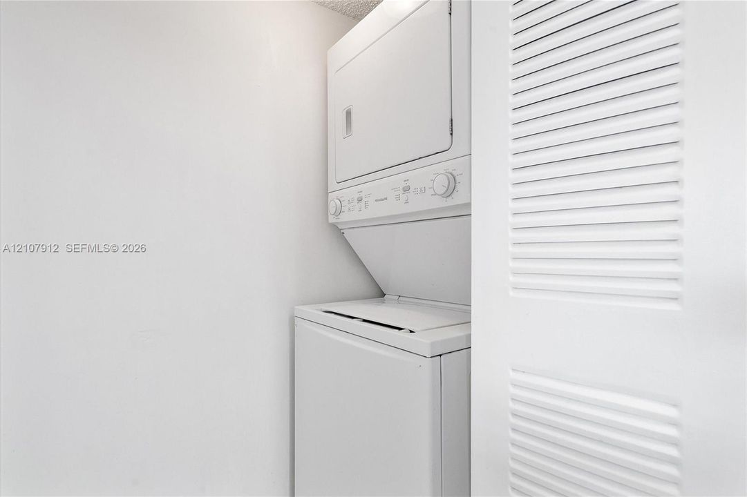 Stacked laundry unit housed within a closet featuring white louvered bi-fold doors