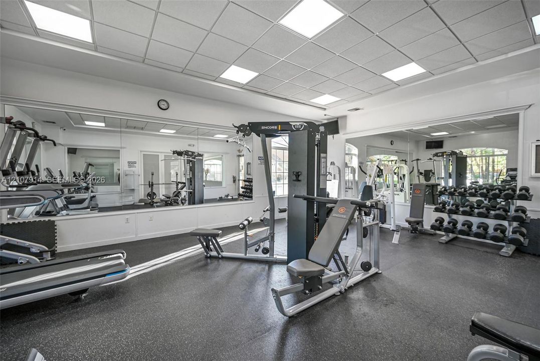 Fitness center featuring wall-to-wall mirrors, recessed grid ceiling lighting, and durable rubberized flooring