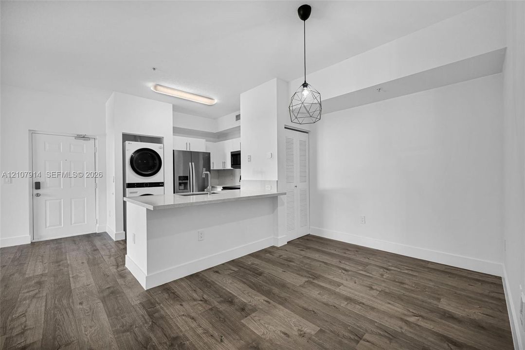 Kitchen featuring a breakfast bar with stone-surfaced countertop, stainless steel refrigerator, integrated laundry center, wood-finish flooring, and geometric pendant lighting