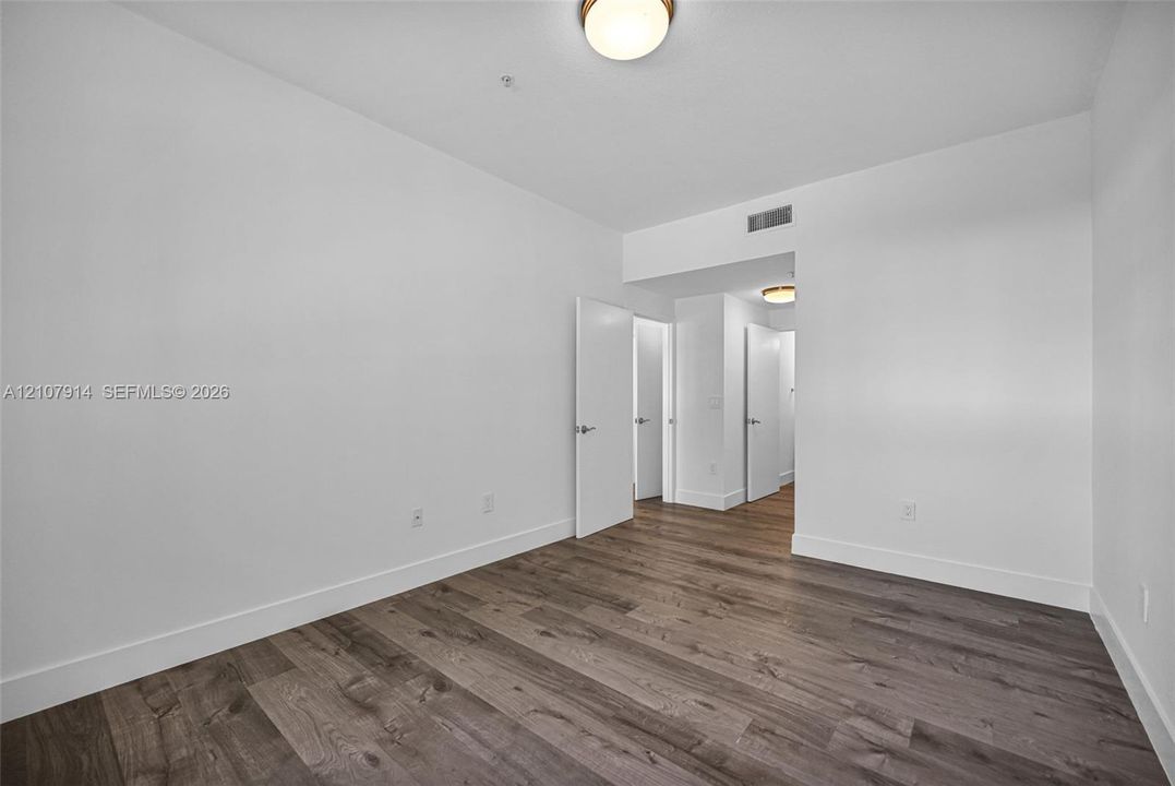Room interior featuring wood-finish flooring, crisp white walls, and flush-mount lighting fixtures