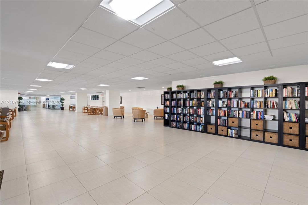 Expansive open-concept space featuring large-format tile flooring, recessed grid ceiling, integrated square lighting panels, and extensive floor-to-ceiling built-in shelving