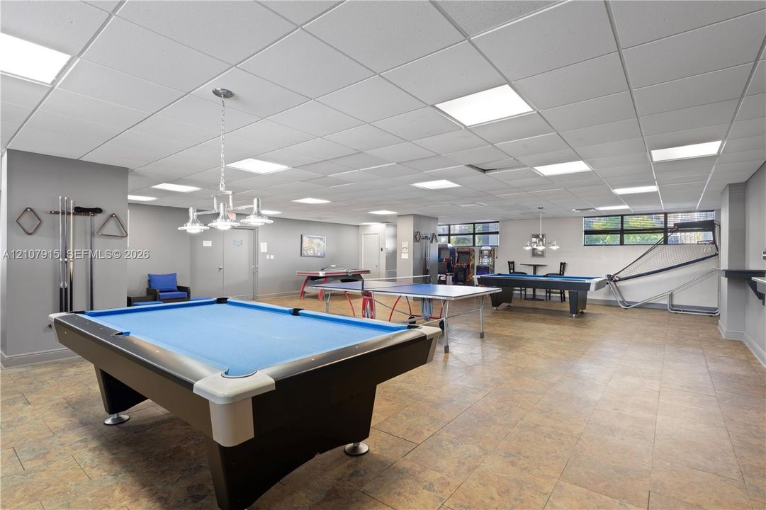 Expansive recreation area featuring recessed ceiling tile grid, neutral wall finishes, tile flooring, and multi-light hanging fixtures