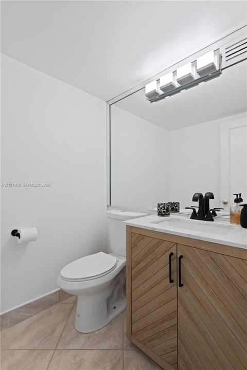Vanity featuring wood-grain cabinet doors in a chevron pattern, light-toned stone countertop, integrated sink, matte black hardware, and an expansive wall-mounted mirror