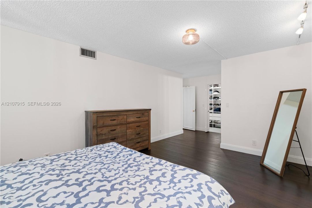 Dark wood-finish flooring and a walk-in closet featuring built-in shelving