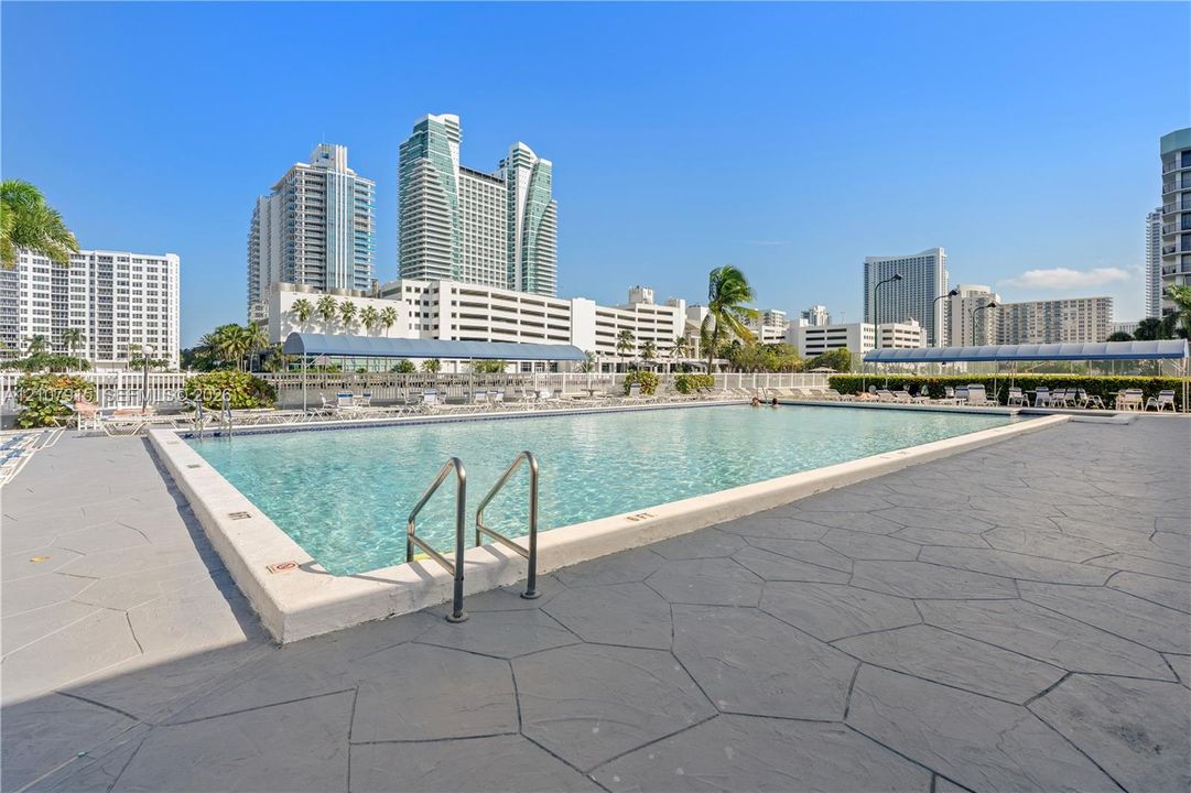 Swimming pool with stone-patterned decking, metal perimeter fencing, and concrete coping