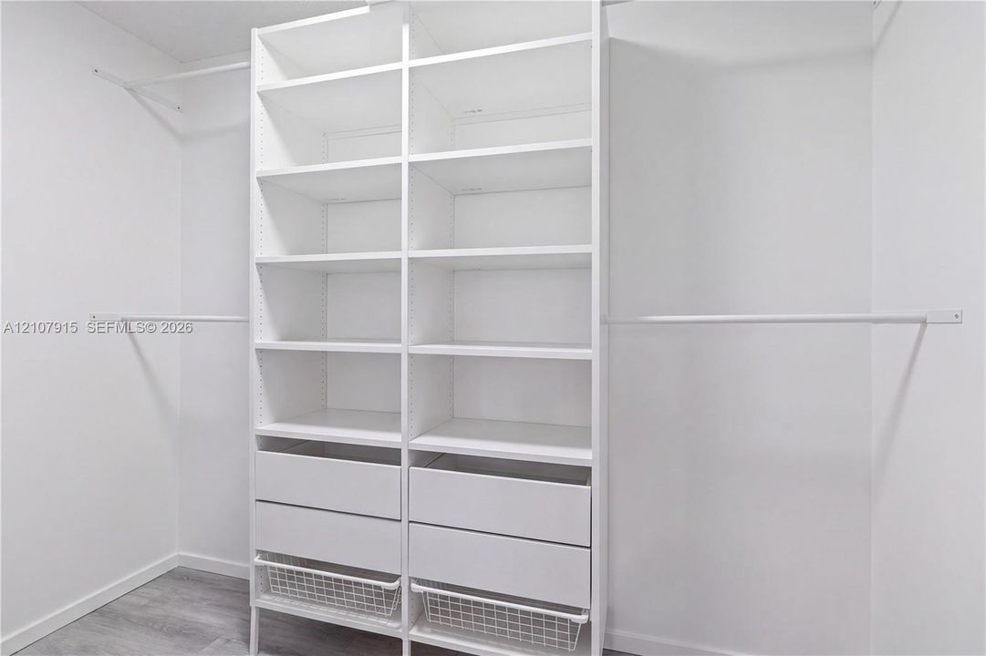Custom white built-in shelving unit featuring adjustable storage racks, dual integrated drawers, wire sliding baskets, and dual metal hanging rods