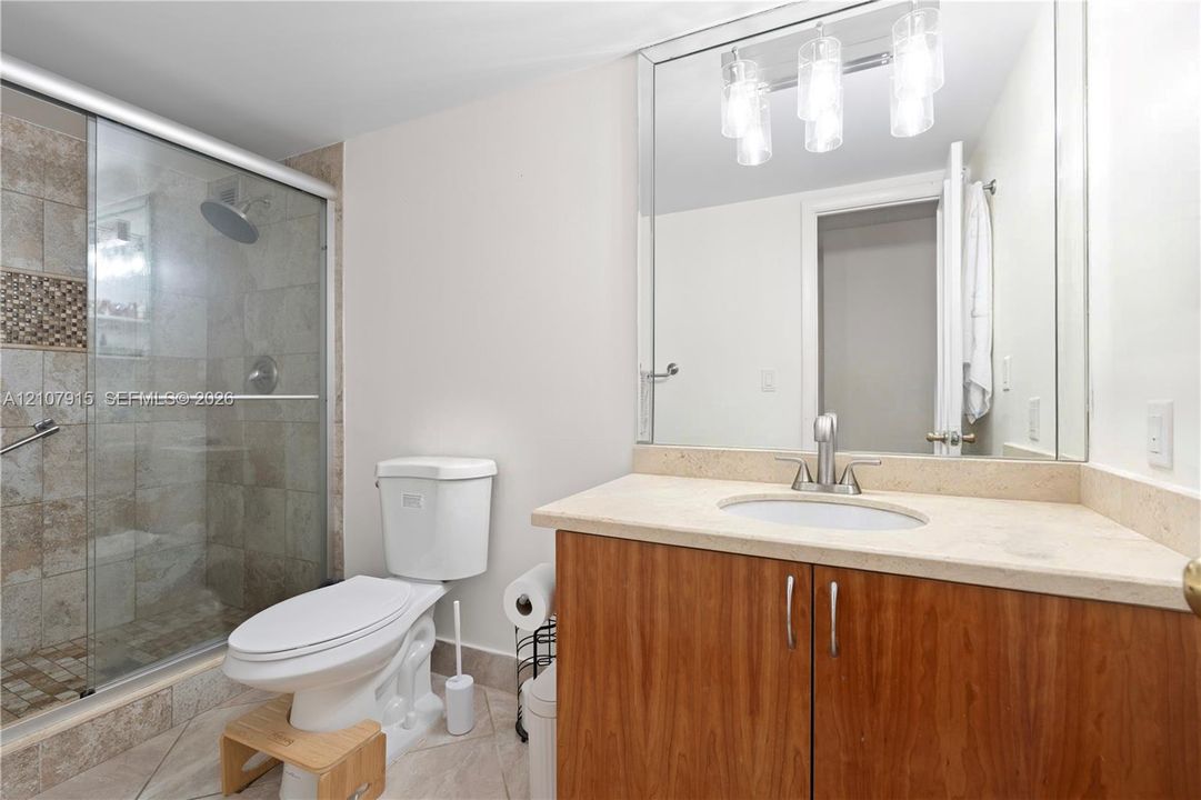 Vanity featuring a light-toned stone countertop, wood-finish cabinetry, a large wall-mounted mirror, and a three-bulb light fixture