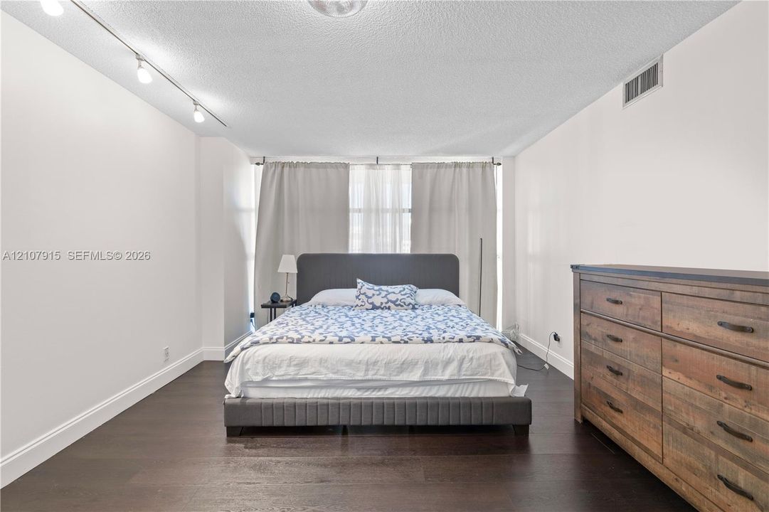 Spacious interior featuring dark wood-finish flooring, adjustable track lighting, and expansive window coverage with full-length drapery