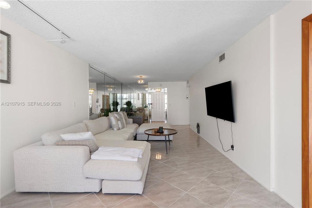 Spacious room featuring neutral tile flooring laid on a diagonal, full-height wall-mounted mirror paneling, textured ceiling, and track lighting