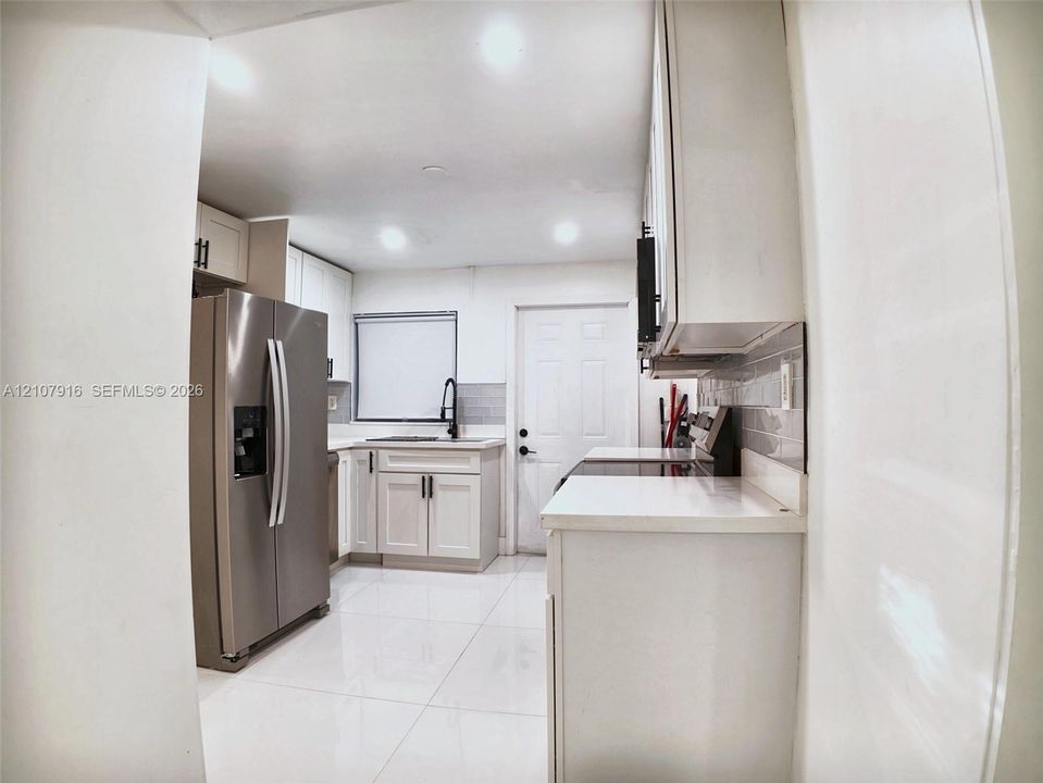 Kitchen featuring white Shaker-style cabinetry, stainless steel side-by-side refrigerator, subway tile backsplash, solid-surface countertops, and large-format tile flooring