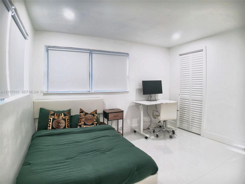 Room featuring polished neutral tile flooring, recessed ceiling lighting, dual windows with roller shades, and white louvered closet doors