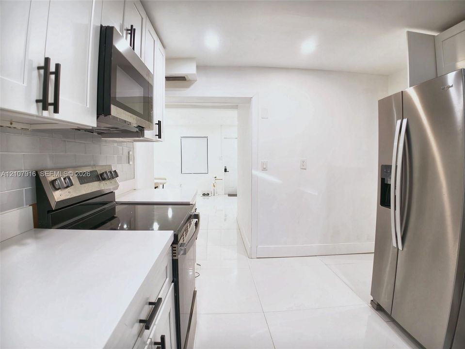 Kitchen featuring white shaker-style cabinetry, stainless steel appliances, subway tile backsplash, solid-surface countertops, and polished tile flooring