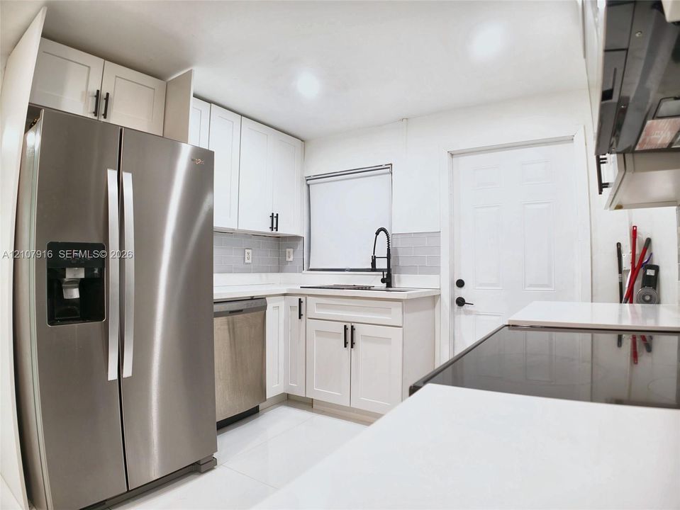 Kitchen featuring white Shaker-style cabinetry, stainless steel appliances, quartz countertops, gray subway tile backsplash, and matte black hardware