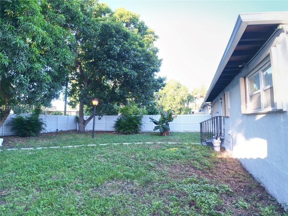 Spacious backyard with mature shade trees, white privacy fencing, and level lawn