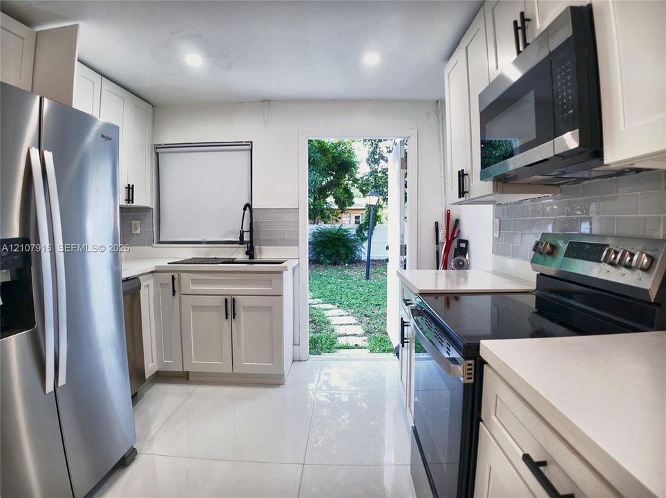 Kitchen featuring white shaker cabinetry, stainless steel appliances, light-toned stone-finish countertops, subway tile backsplash, and polished tile flooring
