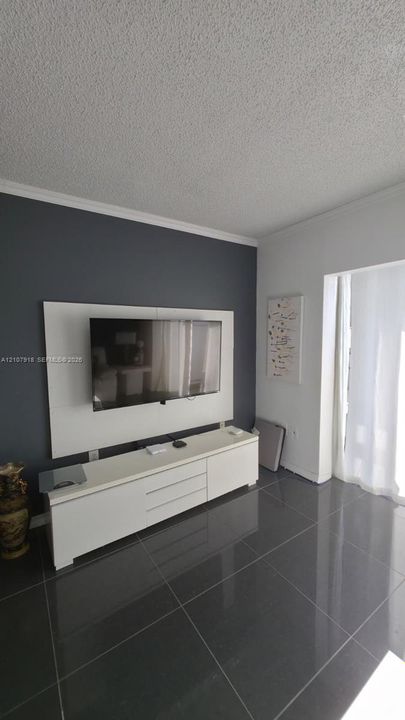 Large-format gray tile flooring, accent wall with built-in white media console, and white crown molding