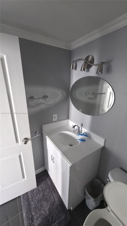 White vanity with an integrated countertop and basin, oval frameless mirror, and brushed-finish three-light vanity fixture