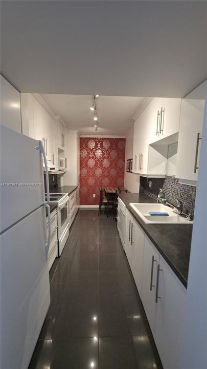 Galley kitchen featuring white cabinetry, dark stone-finish countertops, tile backsplash, track lighting, and ceramic tile flooring