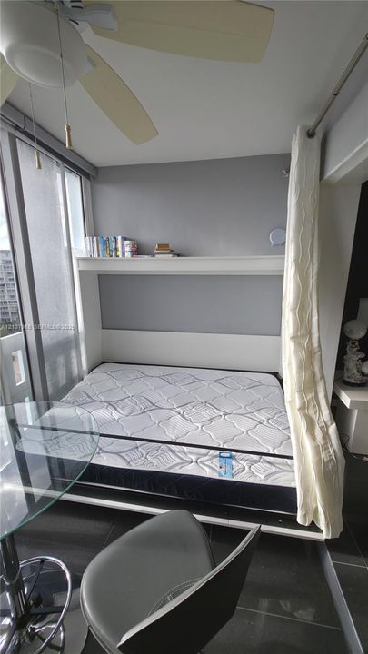 Built-in wall unit featuring an integrated shelf, large windows with floor-to-ceiling glass, polished tile flooring, and a ceiling-mounted light fixture with a fan