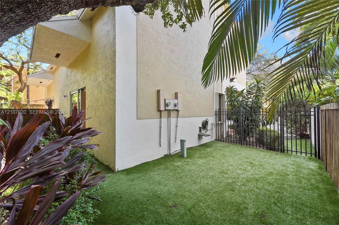 Stucco exterior, fenced yard with synthetic turf, mature landscaping, and sliding glass door entry