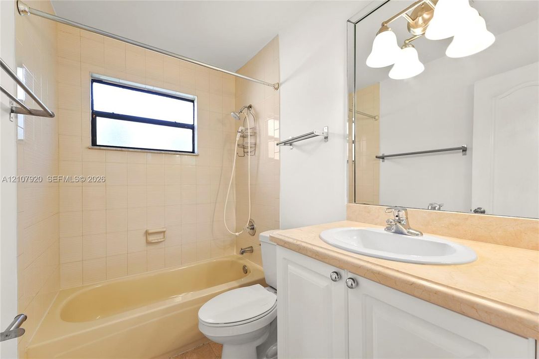 Bathroom featuring a neutral-toned tile shower surround, a built-in tub, a white vanity with a light-colored countertop, and a large-format mirror with integrated three-bulb lighting