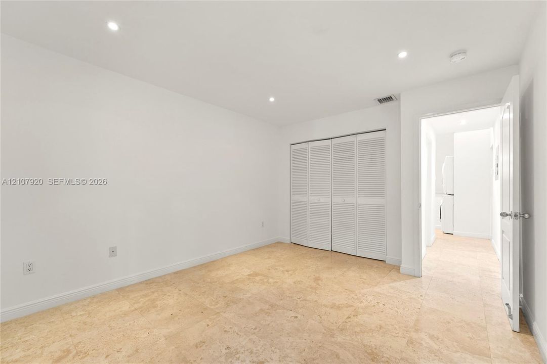 Neutral-toned stone flooring, recessed ceiling lighting, and a multi-panel closet with louvered doors